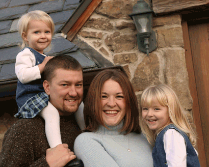 Mother and Father with two young daughters in front of their stone house