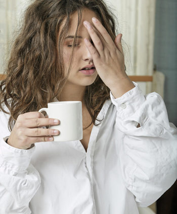 Woman in nightdress holding her head and a cup of coffee