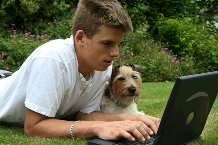 Boy working on laptop in garden with dog