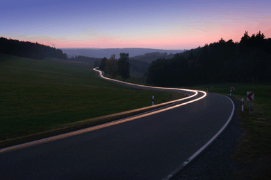 Macadam road winding through country with car light streaming