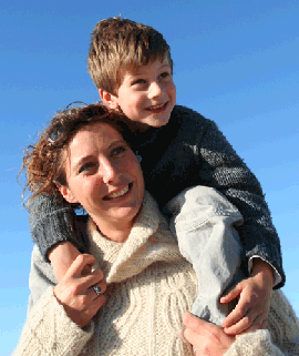 Mom in sweater carrying son on her shoulders and smiling