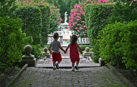 Two children holding hands approach English garden 