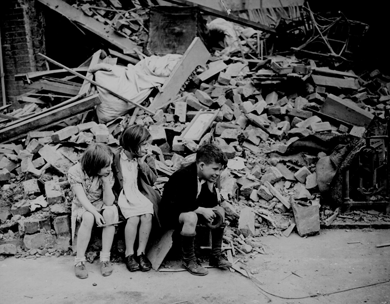 British children sit in the ruins of their London home, bombed by the Nazis during the Blitz